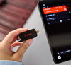 A hand holds a SANDISK USB-C Flash Drive - 256 GB next to a smartphone screen showing audio controls