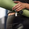 A close-up lifestyle shot of a person holding a rolled-up green textured yoga mat while wearing a black remote control attached to a keyring with a SanDisk Ultra Luxe USB Type-C Flash Drive - 256 GB