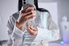 Person holding a smartphone with a SanDisk Phone Drive 256 GB Arctic White USB-C attached, against a blurred indoor background
