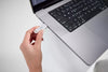 Hand holding a SanDisk Phone Drive 256 GB Arctic White USB-C drive approaching a laptop on a light gray background